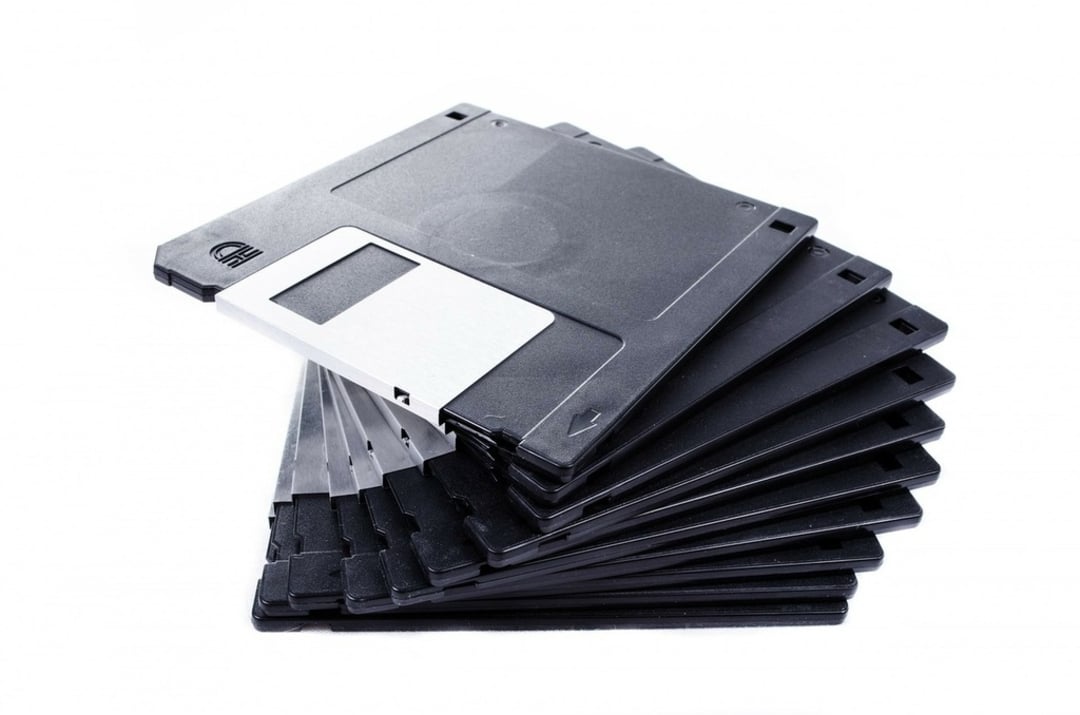 A stack of black 3.5-inch floppy disks is fanned out on a white background, with one disk prominently on top showing its metal shutter.