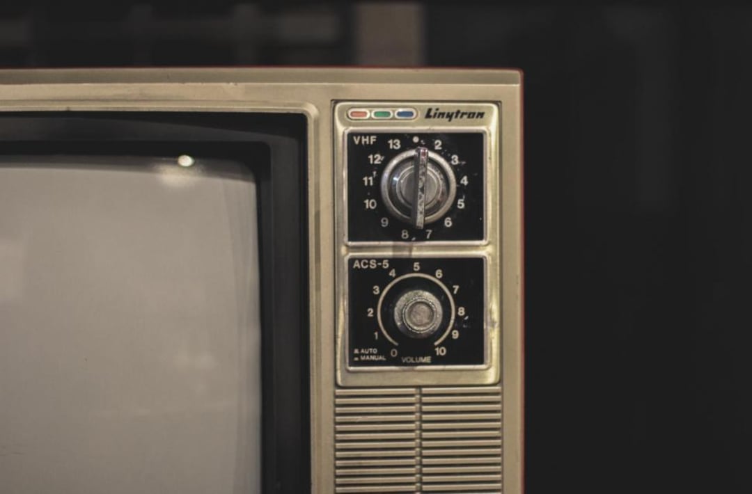Close-up of an old television showing two dials—one for channel selection and one for volume—and the brand name "Linytron" above the dials. The left side of the TV screen is partially visible.