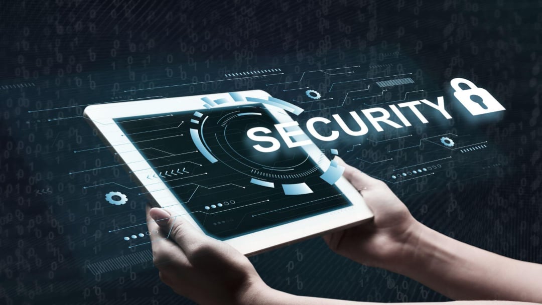 Hands holding a tablet displaying a digital security interface with the word "SECURITY" and a padlock icon, surrounded by futuristic graphics and binary code on a dark background.