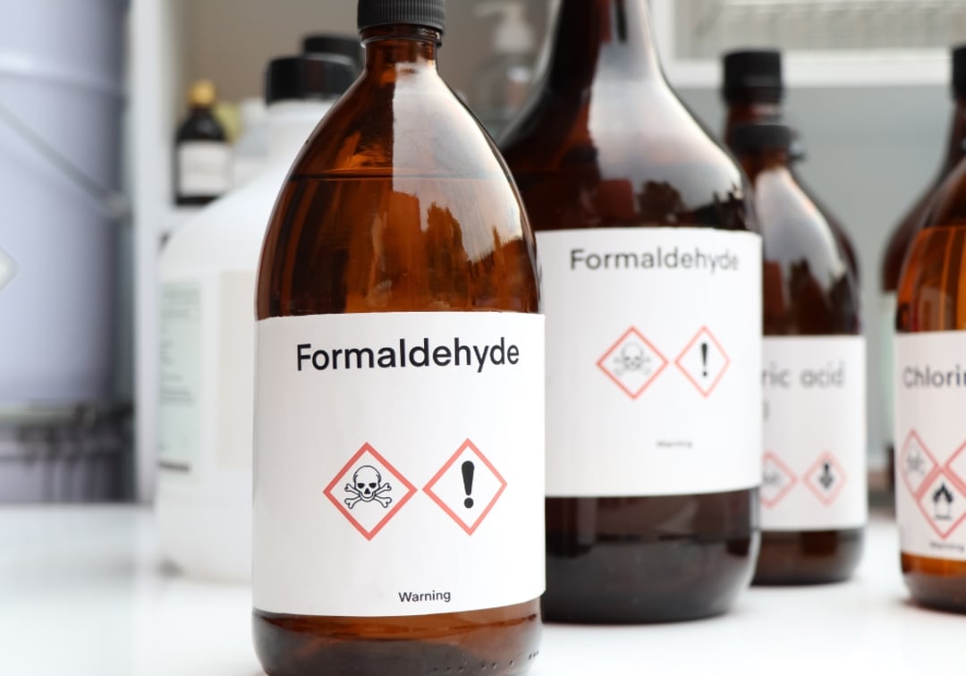 Several brown glass bottles labeled "Formaldehyde" with hazard symbols, including a skull and crossbones and an exclamation mark, are grouped together on a white surface in a laboratory setting.