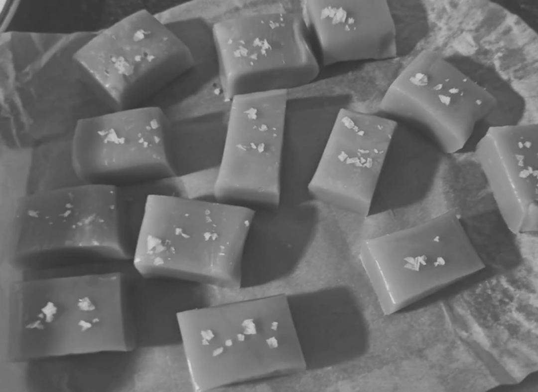 Rectangular caramel candies topped with flaky sea salt, arranged on brown parchment paper.