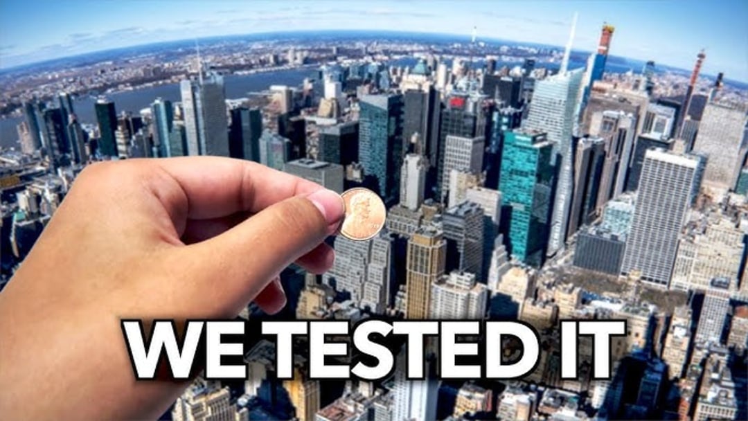A hand holding a penny above a cityscape with tall skyscrapers, as if about to drop it, with large text at the bottom reading "WE TESTED IT.