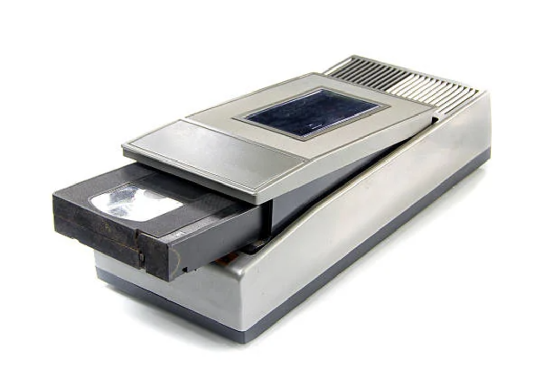 A close-up of a vintage slide projector with a photographic slide partially inserted, displayed on a white background.