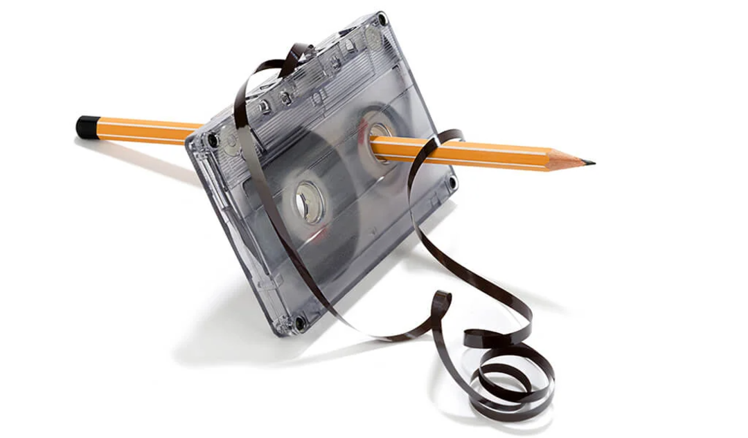 A cassette tape with its brown magnetic tape unraveled and a yellow pencil inserted through one of the reels, commonly used to manually rewind the tape. The image is set against a white background.