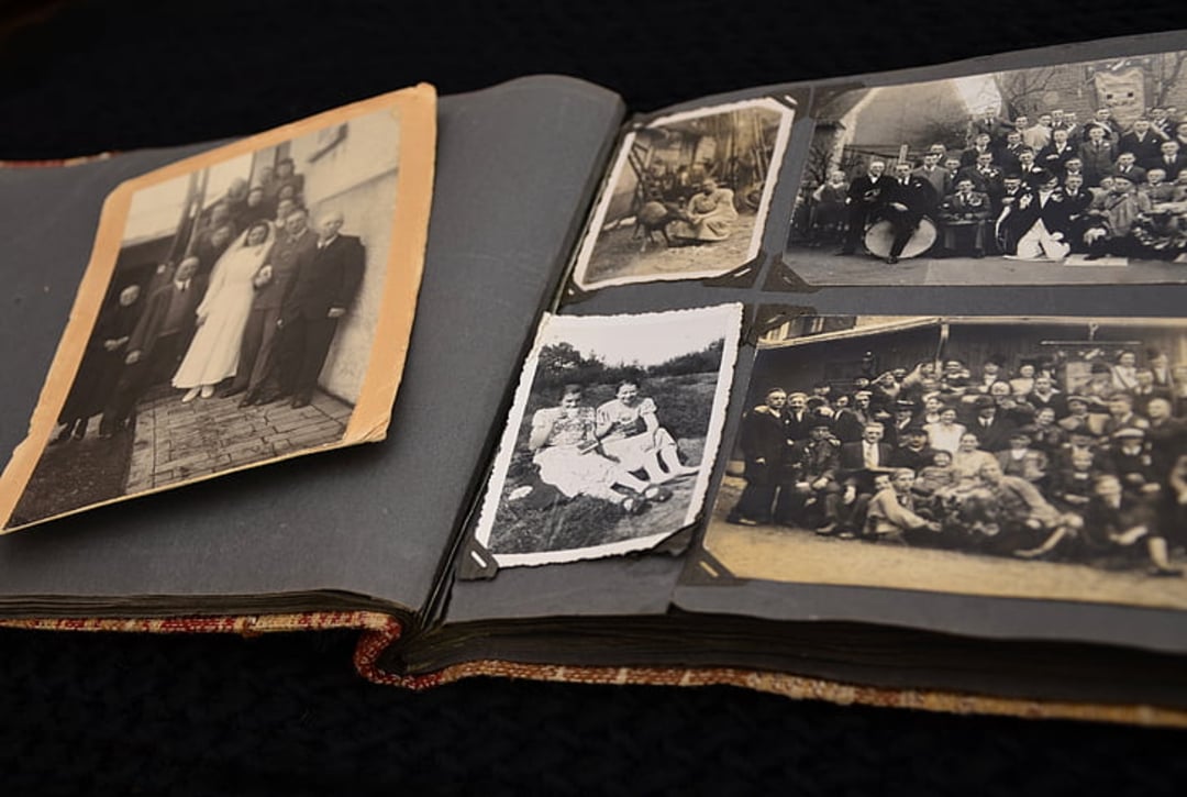 An open photo album displays several old black-and-white photographs, including group portraits and a wedding photo, laid out on a dark textured surface.