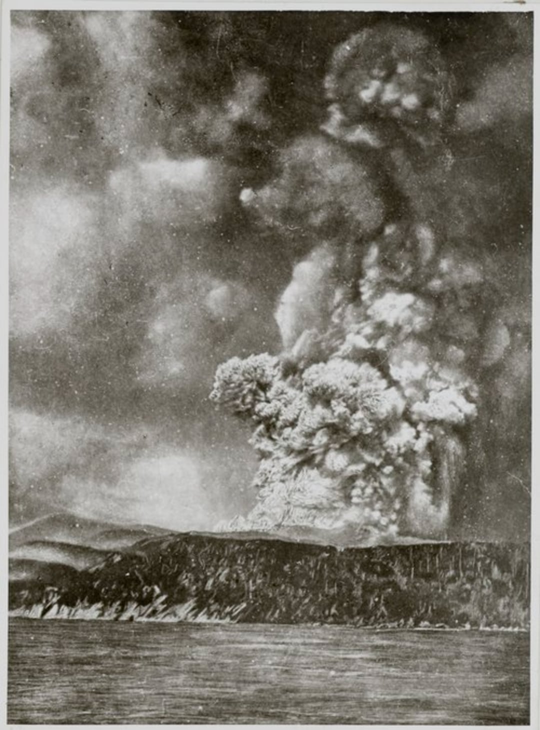 A large volcanic eruption sends a massive plume of ash and smoke high into the sky above a dark, rugged coastline, with water in the foreground and dramatic clouds filling the scene.