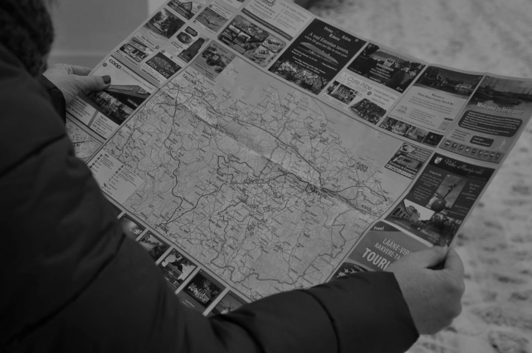 A person in a dark jacket holds and examines a large paper map featuring detailed roads and advertisements, with a snowy ground visible in the background.