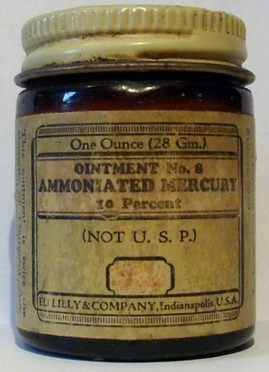 A vintage brown glass jar labeled "Ointment No. 8 Ammoniated Mercury 10 Percent (Not U.S.P.)" by Eli Lilly & Company, Indianapolis, USA. The jar contains 1 ounce (28 gm) of ointment.