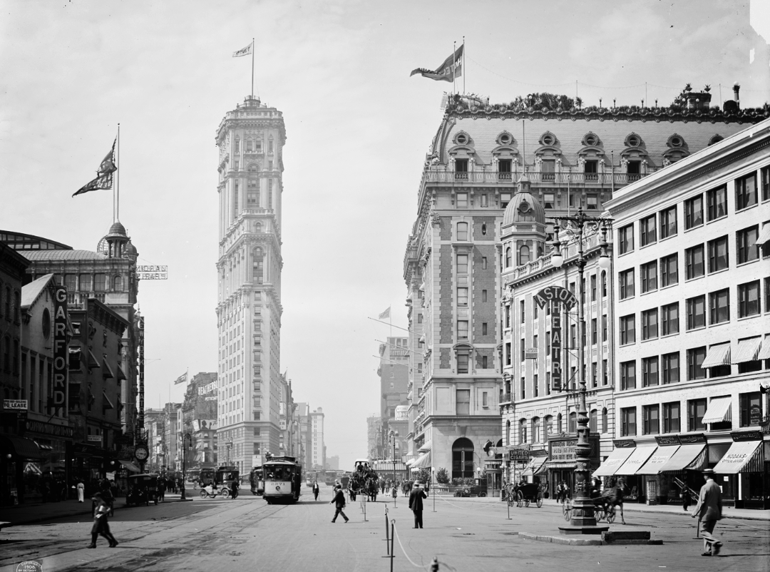 Black and white photo of Times Square, New York City, circa early 1900s, showing vintage cars, trolleys, pedestrians, and tall historic buildings, including the Times Building and the Astor Hotel.