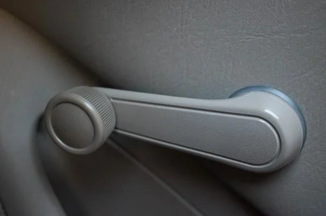 A close-up of a manual car window crank handle on a gray car door panel.