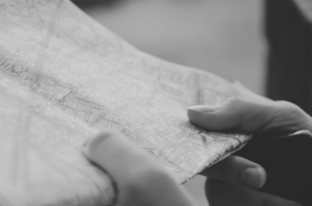 A close-up, black and white photo of hands holding and examining a folded city map, with street names and lines visible but not readable.