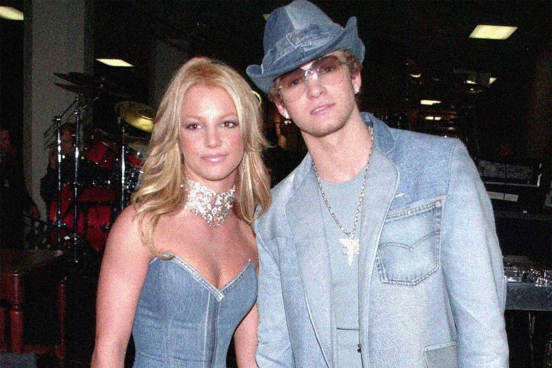 A woman and a man pose together wearing matching denim outfits; the woman has long blonde hair and a strapless denim dress, while the man wears a denim jacket, jeans, and a denim hat with glasses.