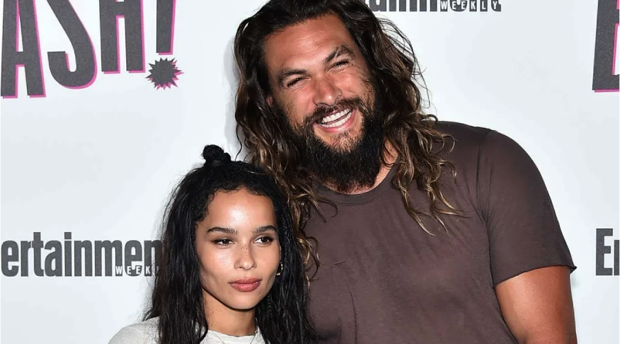 Two people pose together at an Entertainment Weekly event. The person on the left has long dark hair and a neutral expression, while the person on the right has long wavy hair, a beard, and is smiling with an arm around the other.
