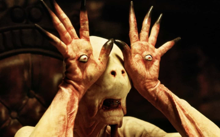 A pale, humanoid creature with eyes embedded in its hands holds its palms up to its face, long black claws extended, creating an eerie and unsettling appearance in a dimly lit setting.