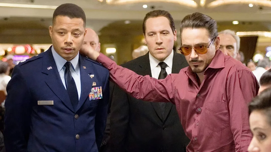 A man in a military uniform stands next to a man in a red shirt with sunglasses who is leaning on his shoulder, while a third man in a black suit looks on in a casino setting.