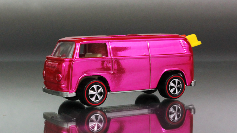 A shiny pink toy van with black and red wheels and a small yellow surfboard sticking out the back, shown on a reflective surface with a gray background.