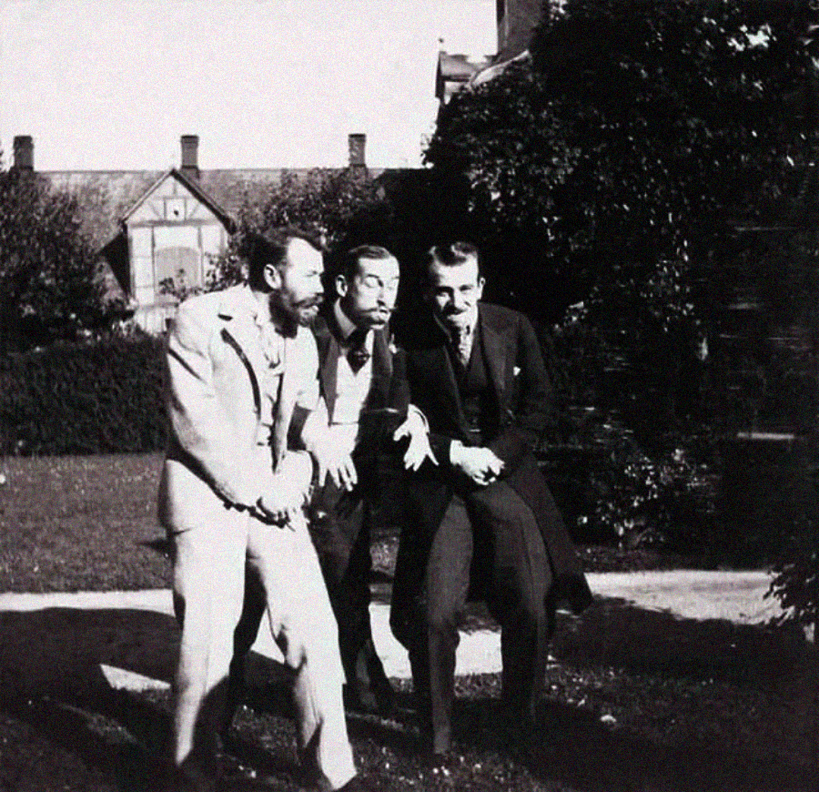 Three men in old-fashioned suits laugh and pose playfully together outdoors on a sunny day, with a large house and greenery in the background.