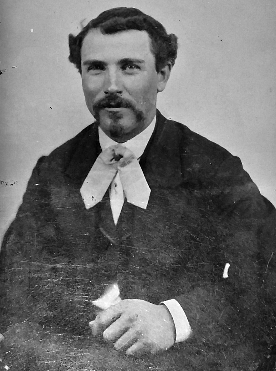 Black-and-white portrait of a man with short dark hair, a mustache, and a goatee, dressed in a suit with a white shirt and a large ribbon-like bow tie, looking at the camera.