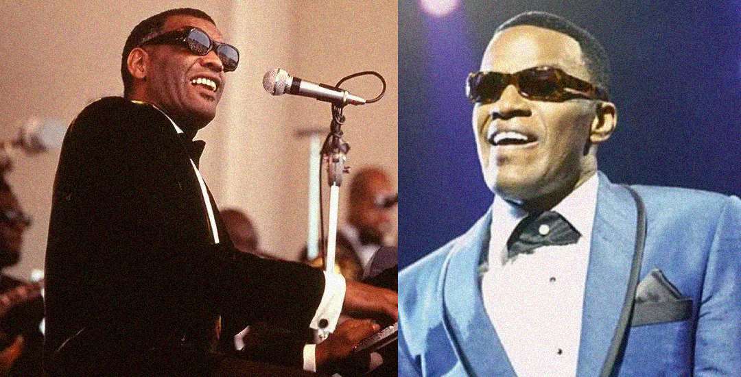 Two men wearing sunglasses and tuxedos perform on stage; the man on the left plays a keyboard and sings into a microphone, while the man on the right smiles and stands in a blue suit and bowtie.
