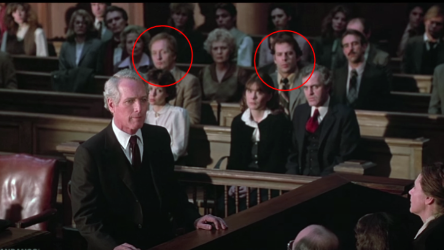 A courtroom scene with a lawyer speaking at the front. The audience is seated in pews behind him, with two individuals in the jury box highlighted by red circles. The mood appears serious and attentive.