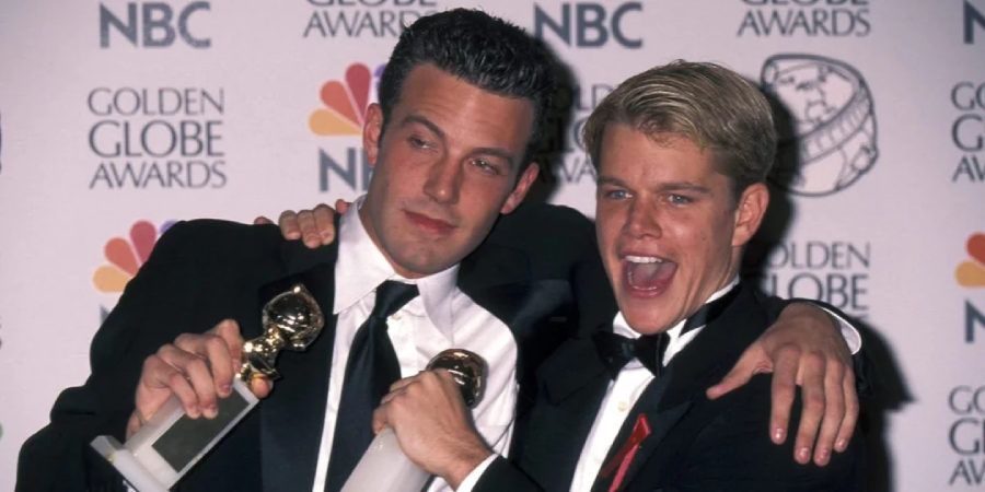 Two men in tuxedos smile and pose with their arms around each other, each holding a Golden Globe award, standing in front of a backdrop with Golden Globe Awards and NBC logos.