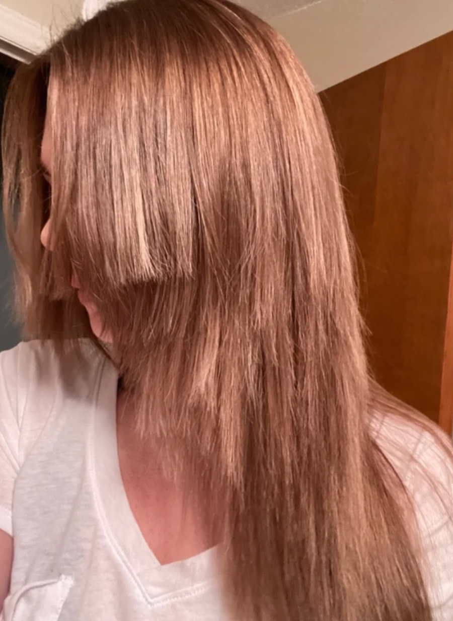 A person with long, light brown hair wearing a white shirt is looking to the side, showing unevenly cut bangs that are much shorter than the rest of their hair.