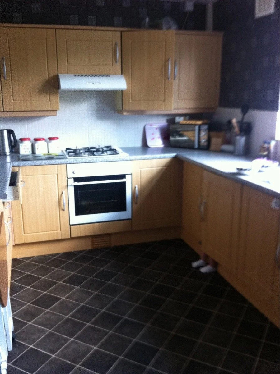 A kitchen with wooden cabinets, a built-in oven, gas stove, and countertop appliances; a pair of small feet are visible peeking out from below a lower cabinet on the right.