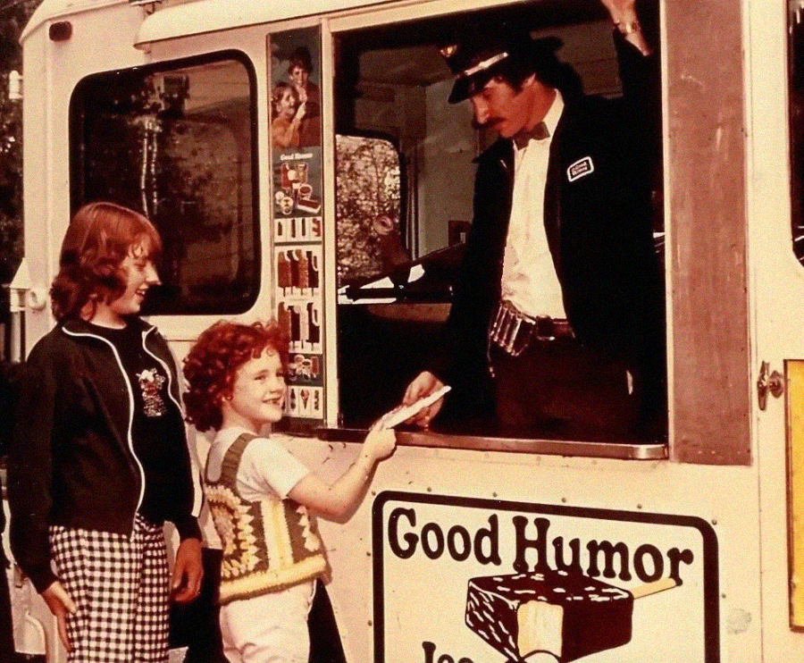 Two children stand at an ice cream truck window, smiling as a uniformed vendor hands them ice cream. The truck displays a "Good Humor Ice Cream" sign.