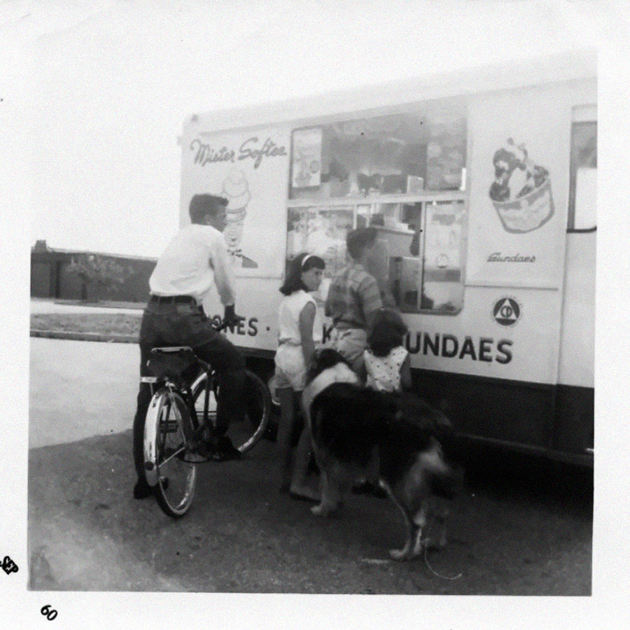 A black-and-white photo shows three children, one dog, and a person on a bicycle gathered at an ice cream truck with "Mister Softee" and sundae images on the side.