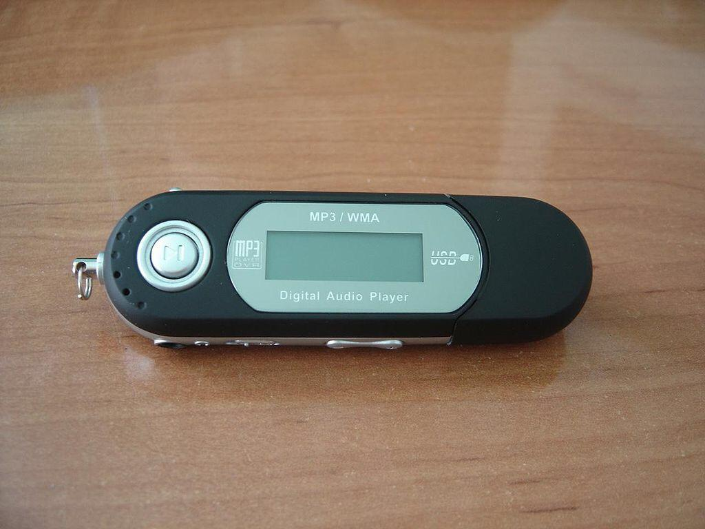A black and silver USB MP3 digital audio player with a small LCD screen and control buttons, lying on a wooden surface.