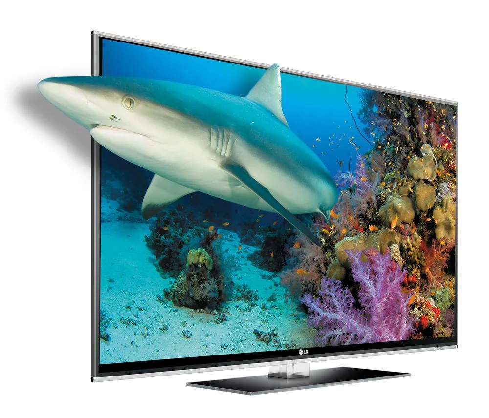 A 3D television displays a vivid underwater scene with a shark appearing to swim out of the screen, alongside colorful coral and ocean life in the background.
