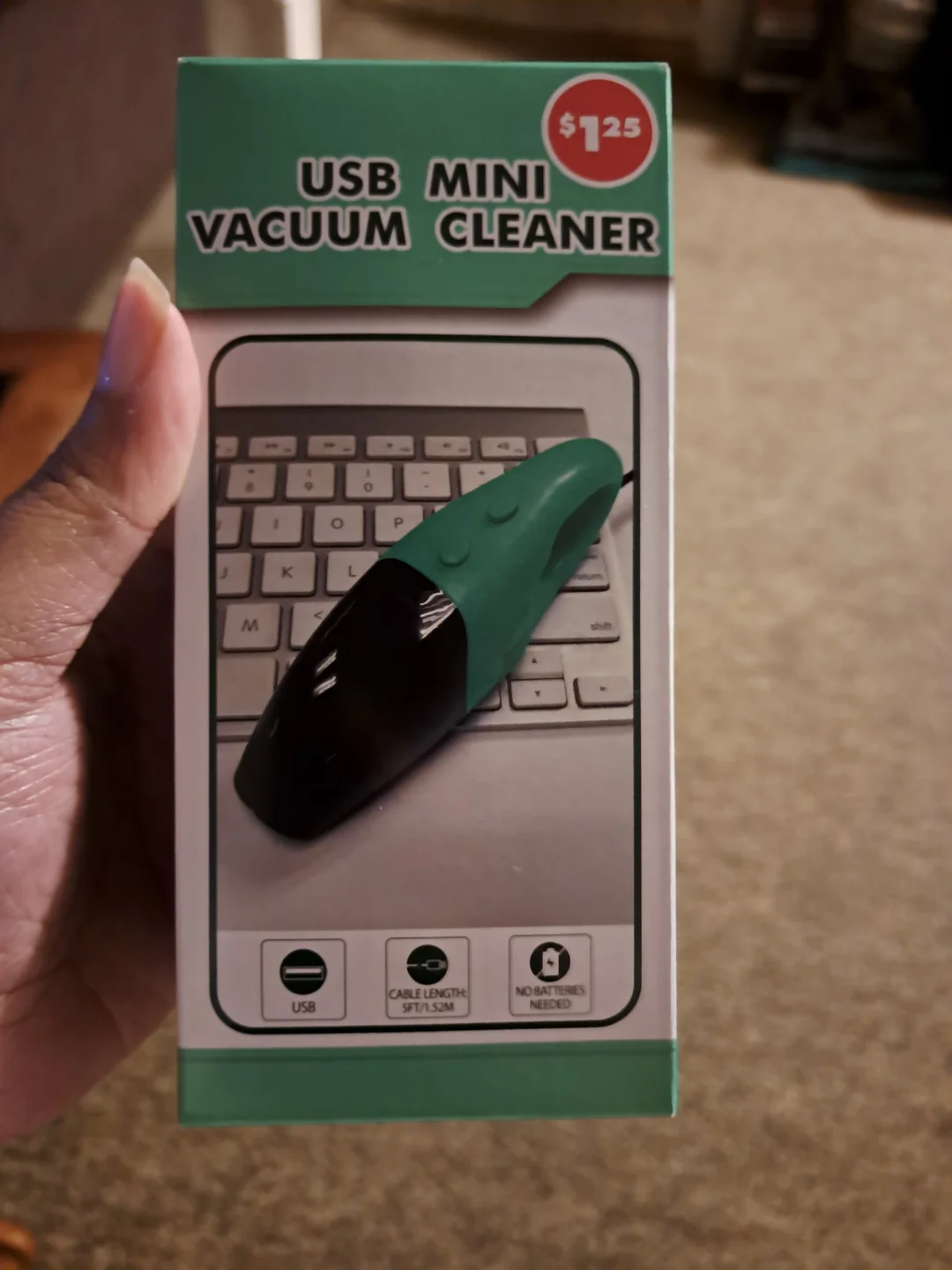 A hand holds a box labeled "USB Mini Vacuum Cleaner" priced at $1.25, showing an image of the small green and black device placed on a computer keyboard. Icons indicate USB use, cable length, and no need for batteries.