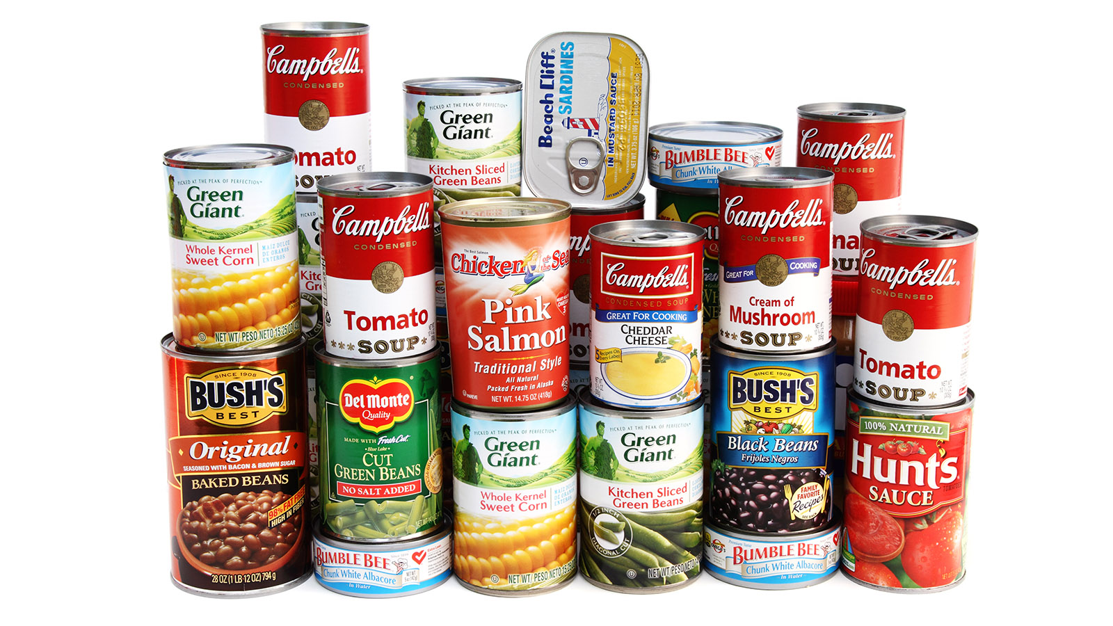 A variety of canned foods including vegetables, soups, beans, salmon, and tuna are stacked together. Brands like Campbell’s, Green Giant, Bush’s Best, Bumble Bee, and Hunt’s are visible on the cans.