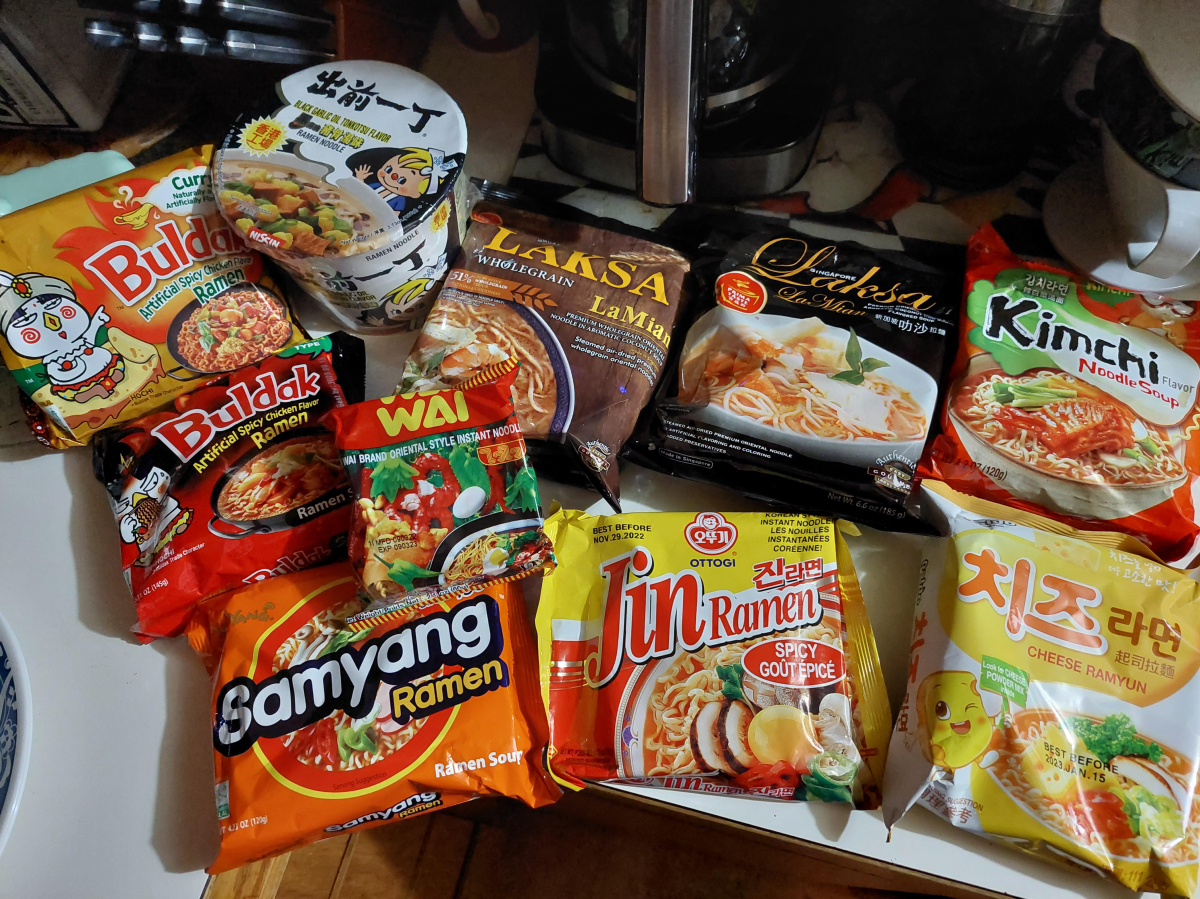 A variety of instant ramen noodle packages in different colors and flavors, including brands like Samyang, Jin Ramen, and Wai, are spread out on a kitchen counter.