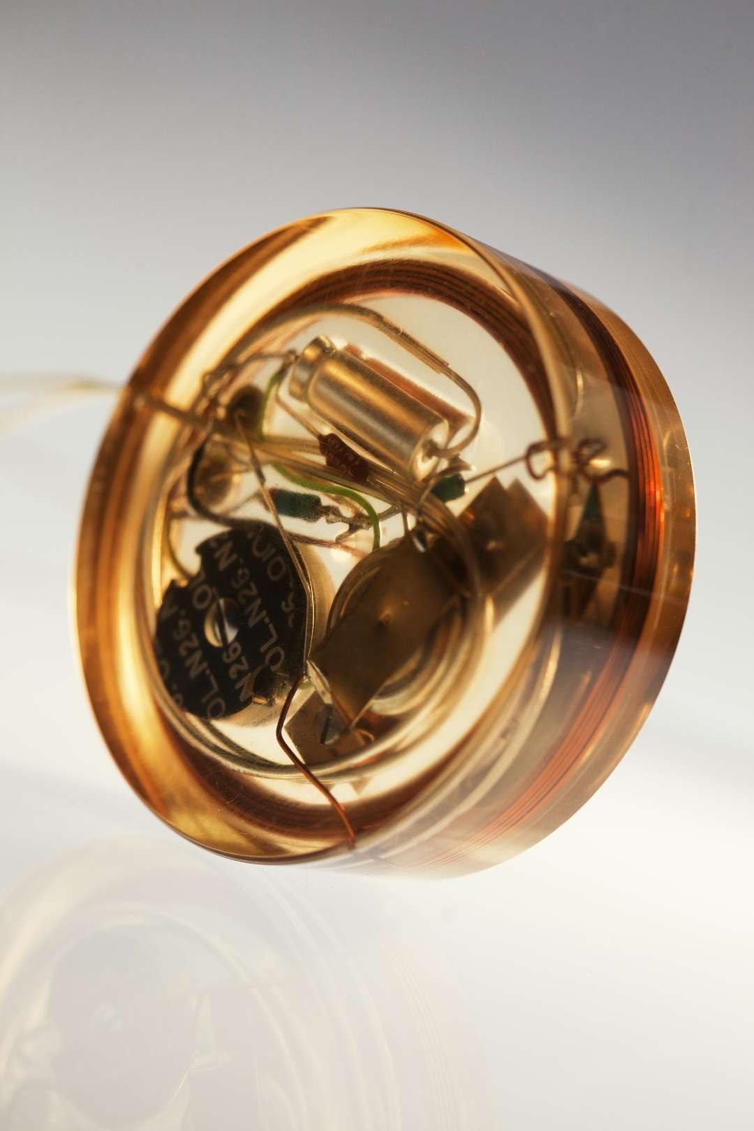 Close-up of a transparent amber-colored electrical component, showing internal coils and wires, set against a softly lit gradient background.