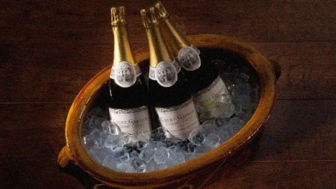 Four bottles of sparkling wine or champagne in a wooden bowl filled with ice, placed on a dark wooden surface.