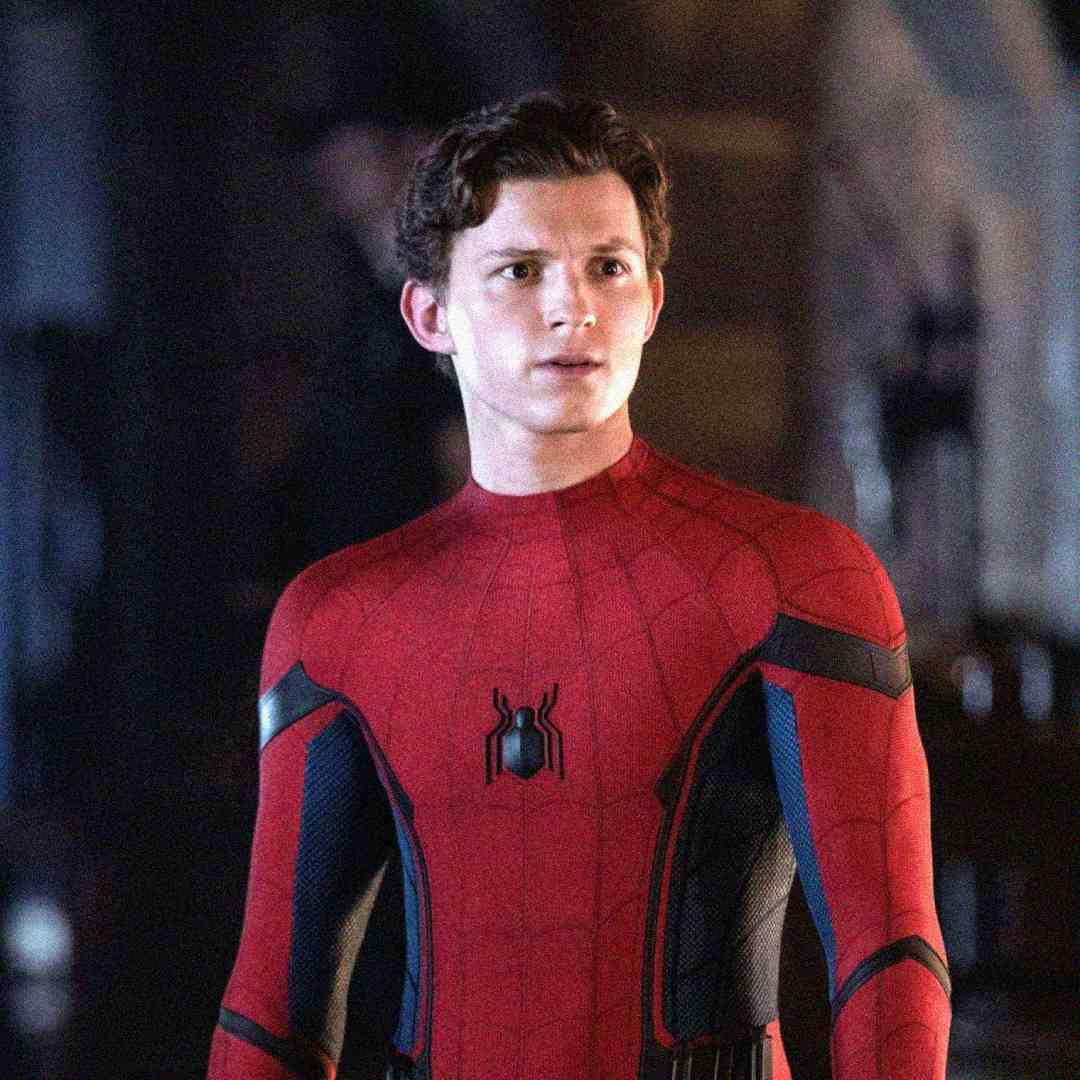 A young man wearing a red and blue Spider-Man suit stands indoors, looking slightly to the side with a concerned expression. The background is dimly lit and blurred.