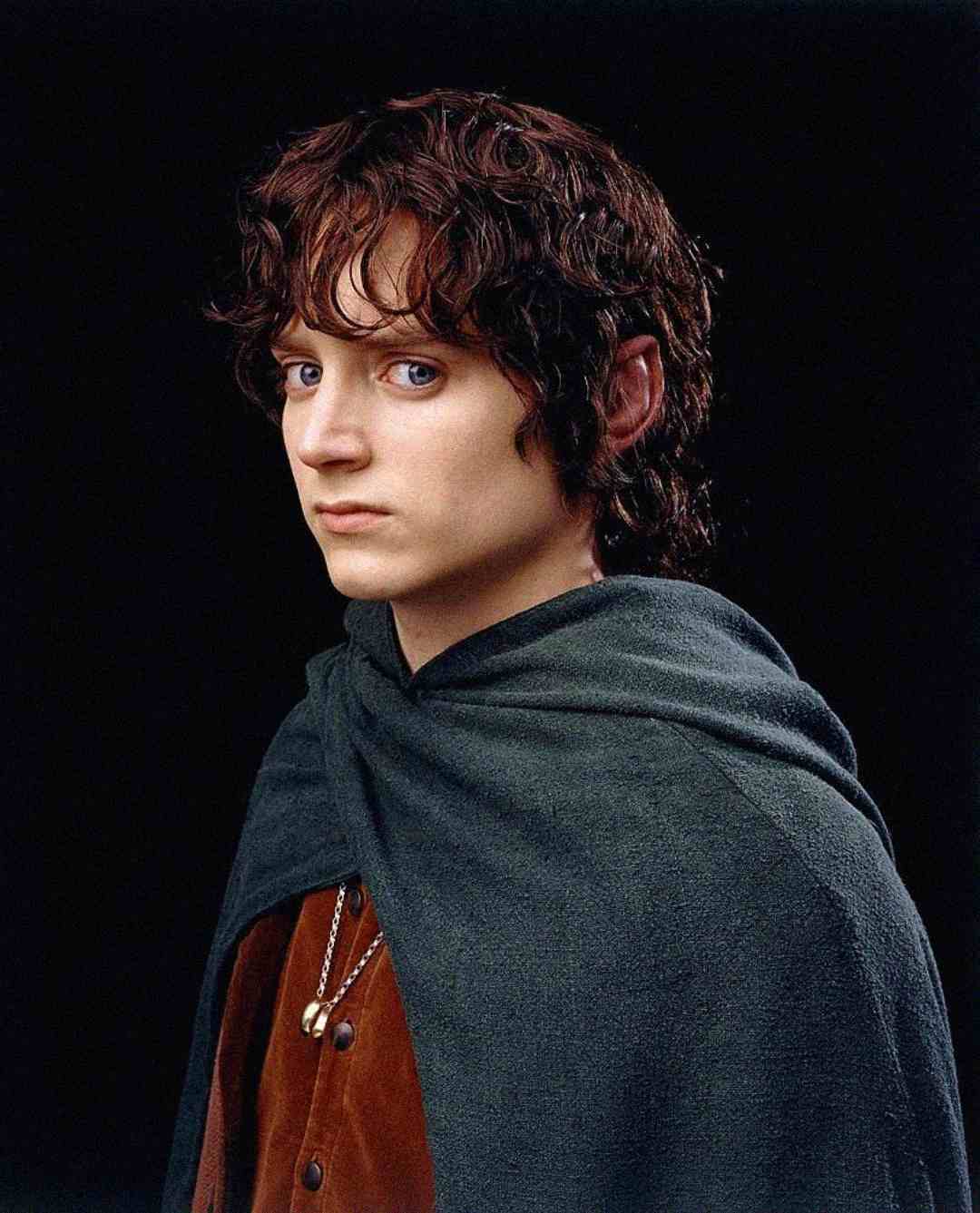 A young person with curly brown hair, pale skin, and blue eyes wears a gray-green cloak over a brown shirt, gazing seriously to the side against a dark background.