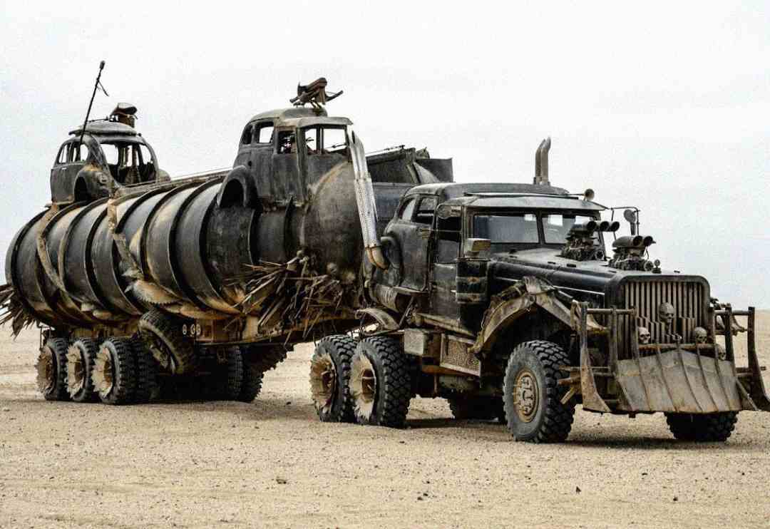 A rugged, heavily modified truck with large tires and a spiked grille pulls a rusted, armored tanker on a barren desert landscape, resembling an apocalyptic vehicle from a dystopian movie.