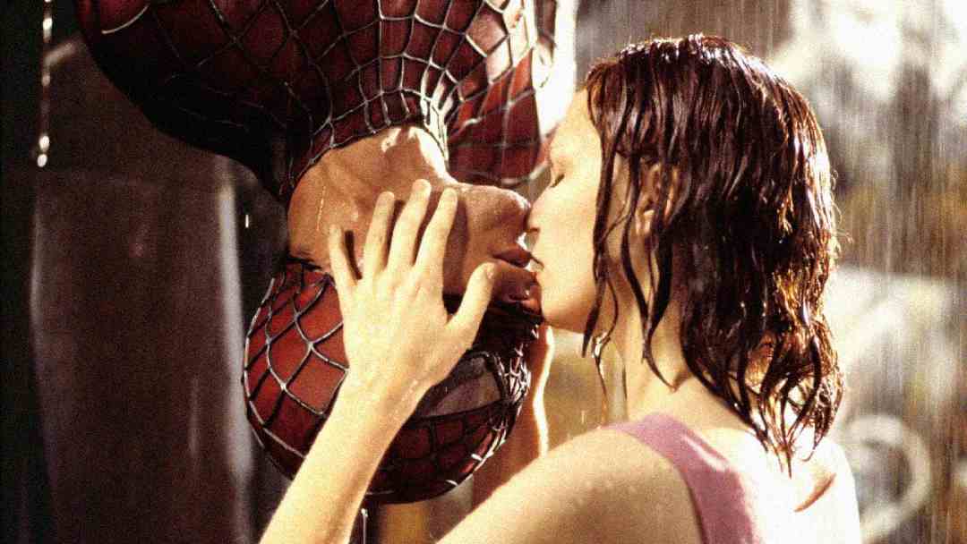 A woman gently kisses Spider-Man, who hangs upside down in his mask, as rain falls around them in a dramatic, intimate moment.