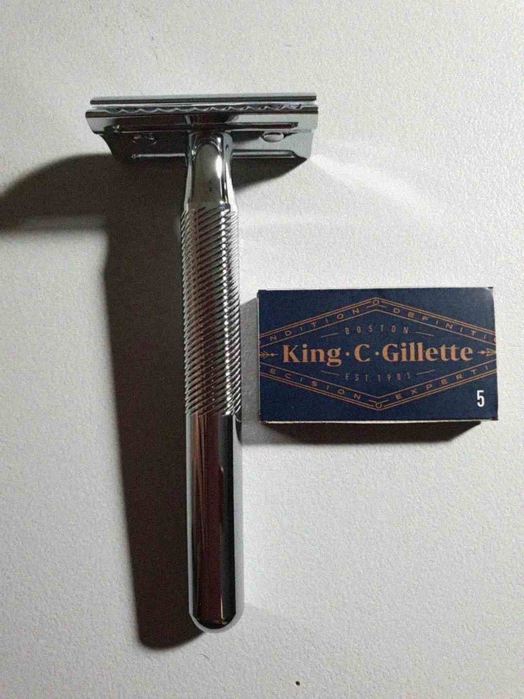 A silver safety razor is placed next to a dark blue box labeled "King C. Gillette" with the number 5 in the corner, on a light-colored surface.