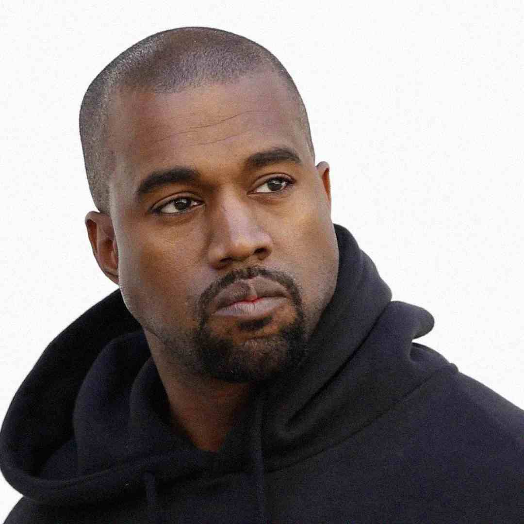 A man with a shaved head and trimmed beard wearing a black hoodie looks slightly to the side against a plain white background.