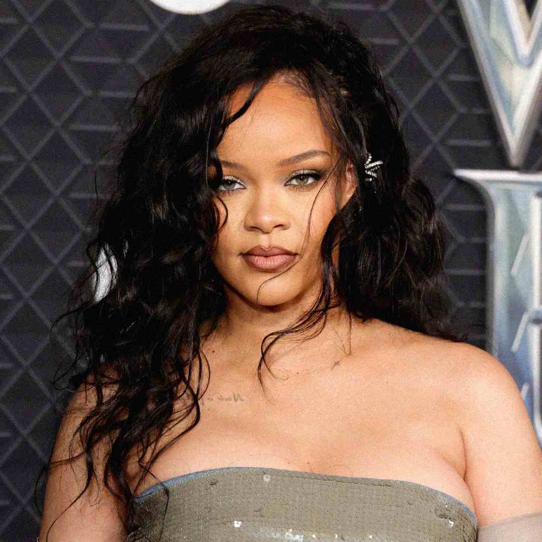 A woman with long wavy dark hair, wearing a strapless silver dress, stands in front of a geometric dark background, looking confidently at the camera.