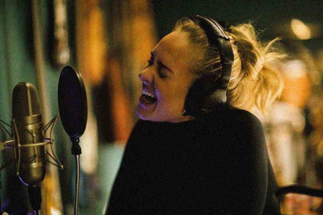 A person wearing headphones passionately sings into a microphone in a recording studio, with eyes closed and mouth wide open, expressing strong emotion.