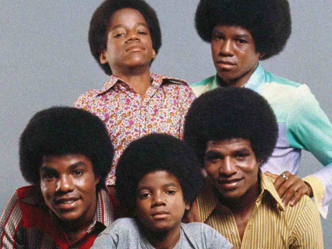 Five young boys with natural afro hairstyles pose together, wearing colorful, patterned 1970s shirts. Three are seated in front, two stand behind them, all smiling or looking confidently at the camera against a plain background.