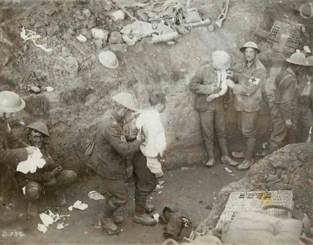 A group of World War I soldiers in a trench tend to wounded comrades; some sit or stand, bandaging injuries, with medical supplies and debris scattered around them.