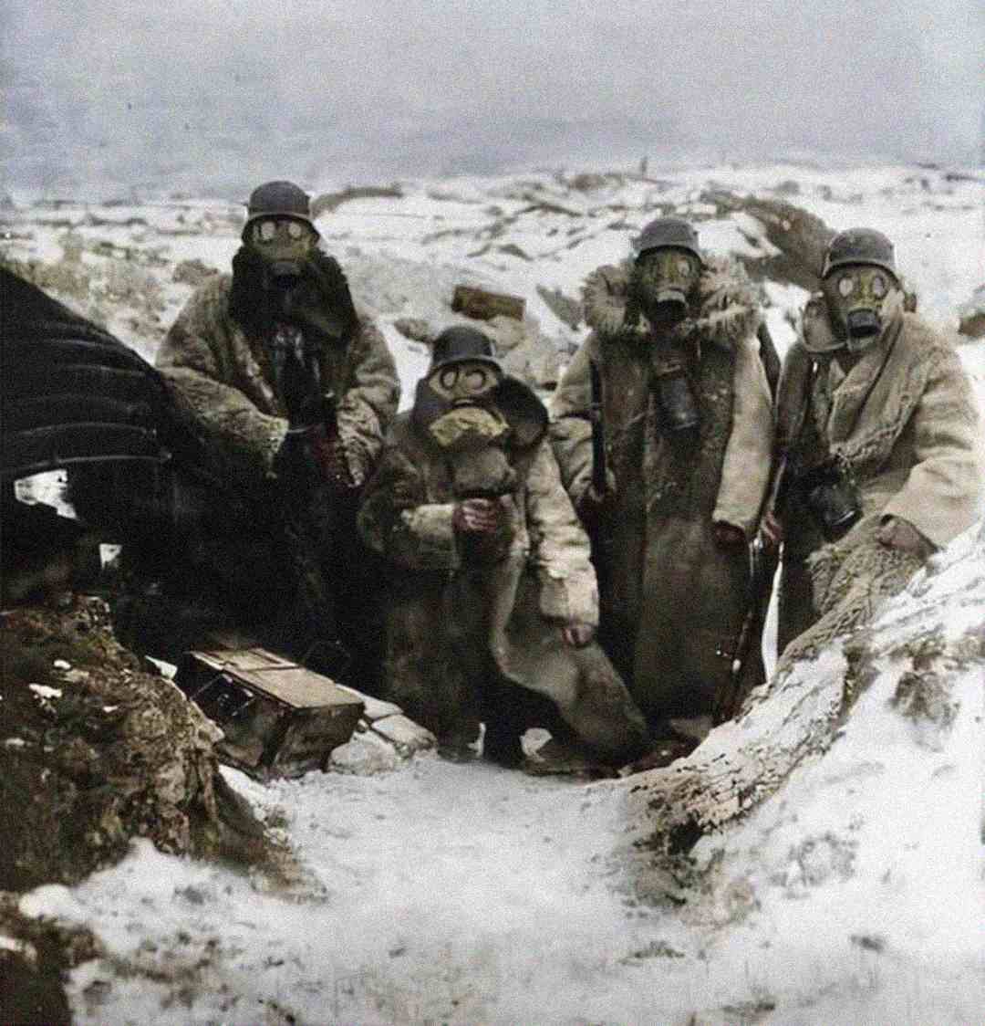Four soldiers in fur coats and gas masks stand in a snowy, barren trench during winter. The landscape is bleak, with snow covering the ground and no vegetation visible.