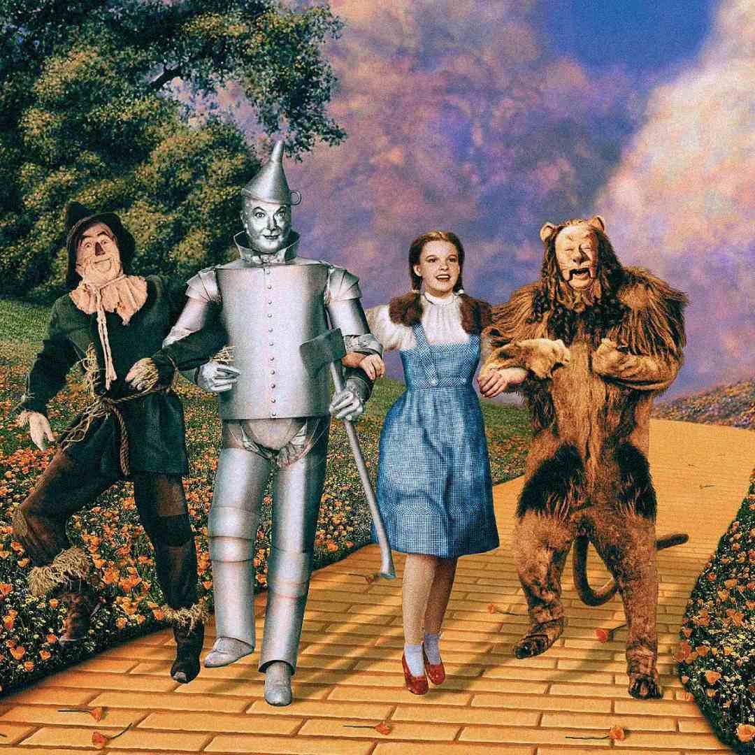 Four characters—a scarecrow, a tin man, a girl in a blue dress, and a lion—walk arm in arm down a yellow brick road surrounded by flowers and greenery under a colorful sky.