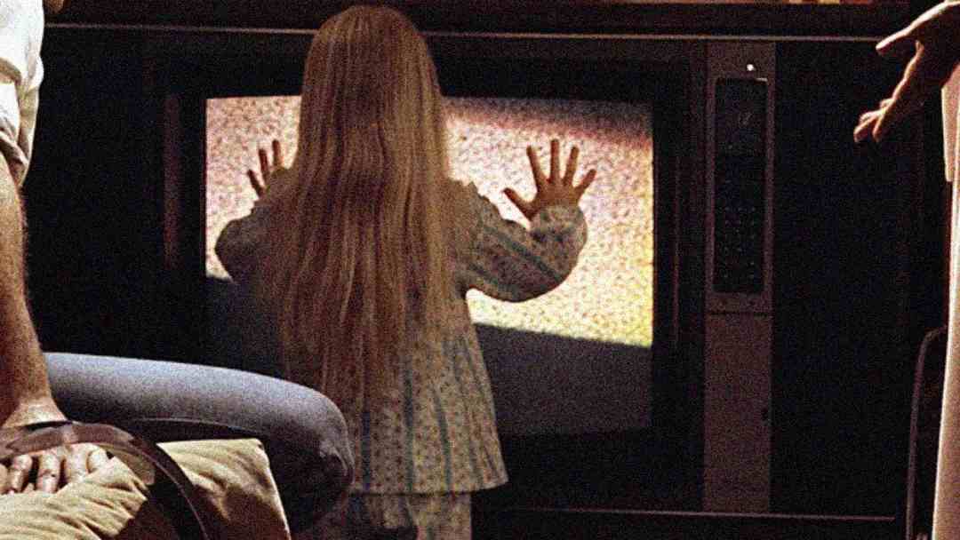A young girl in pajamas stands facing an old television displaying static, with her hands pressed against the screen. Adults are partially visible nearby, watching her closely.