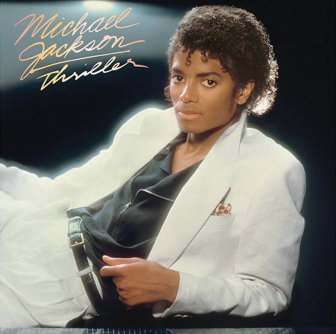 Album cover for Michael Jackson's "Thriller," showing him in a white suit with a black shirt, reclining against a dark background with the album title written in cursive at the top left.